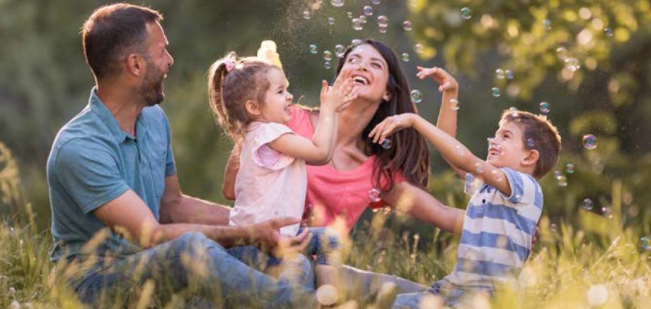Vater, Tochter, Mutter, Sohn sitzen auf einer Wiese und betrachten Seifenblasen.