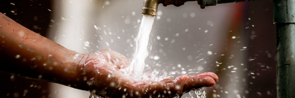 Clean water flows freshly from the tap into the palm of your hand. Focus on the faucet.