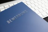 Blaue Mappe mit der Aufschrift Bewerbung liegt auf einerweißen Tastatur.