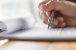 Hand mit silbernem Kugelschreiber füllt ein Formular aus.
