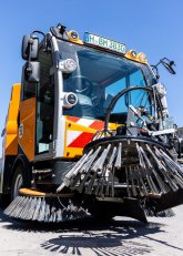 Kehrmaschine des Bauhofs in Großaufnahme aus der Froschperspektive zu sehen. Im Fokus steht eine der großen Bürsten an der Front.