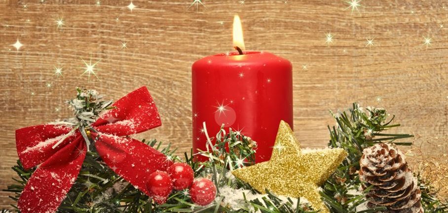 In der Mitte liegt ein grüner Tannenzweig mit roter Schleife, goldenem Stern und braunem Tannenzapfen. Davor liegen 6 rote Kugeln. Alles ist teilweise von Schnee bedeckt. Hinter dem Zweig steht eine brennende rote Kerze. Der Hintergrund ist gemasertes helles Holz.