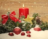 In der Mitte liegt ein grüner Tannenzweig mit roter Schleife, goldenem Stern und braunem Tannenzapfen. Davor liegen 6 rote Kugeln. Alles ist teilweise von Schnee bedeckt. Hinter dem Zweig steht eine brennende rote Kerze. Der Hintergrund ist gemasertes helles Holz.