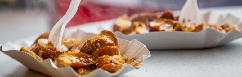 Zwei weiße Pappschalen mit Currywurst. In jeder steckt eine weiße Plastikgabel.