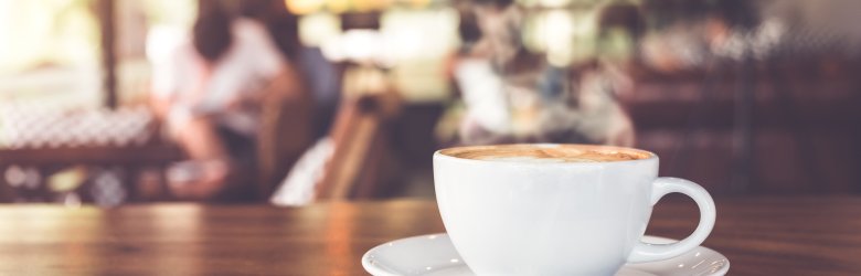Tasse Kaffee auf einem Tisch im Café mit Menschen. Vintage- und Retro-Farbeffekt - geringe Schärfentiefe