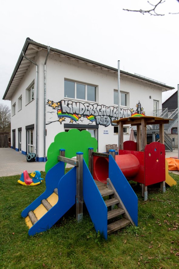 Grün blau rotes Spielplatzgerät im Garten des Kinderschutzbundes im Hintergrund das Gebäude mit bunter Bemalung