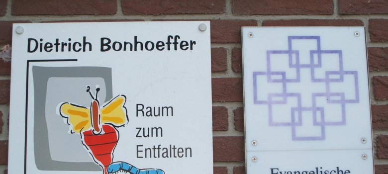 Es ist das Logo der evangelischen Dietrich-Bonhoeffer-Kindertagesstätte zu sehen. Dieses setzt sich aus grauen Rechtecken und einem gelb/roten Schmetterling mit entsprechenden Schriftzug zusammen.