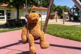 Schaukelbild.jpg Ein großer Teddybär sitzt auf der Schaukel in der Maria-Jockel-Kita im Hintergrund sieht man das Gebäude