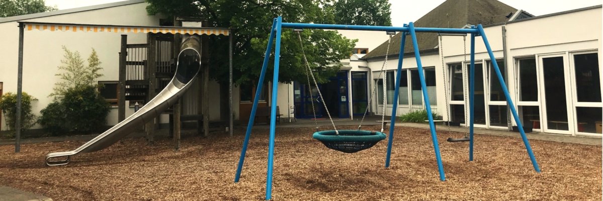 Ein Teil des Außengeländes der Kita ist sichtbar. Man sieht eine Rutsche und eine Korbschaukel