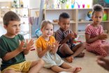 Eine Gruppe von Kindergartenkindern sitzt auf dem Boden. Die Kinder klatschen in die Hände.