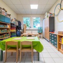 Im Werkräum sind Regale und Schränke mit vielen Materialien. In der Mitte des Bildes sind Werkbänke.