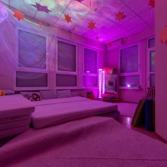 Der Snoozelraum ist ein Entspannungsraum, der abgedunkelt und in leicht lila Licht getaucht ist. Man sieht eine Kissenlandschaft und beruhigendes Licht von einer Wassersäule.