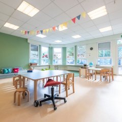 Es ist einer der Gruppenräume der Einrichtung zu sehen. Im Raum stehen Tischgruppen. Durch die helle Fensterfront, wirkt der Raum einladend.