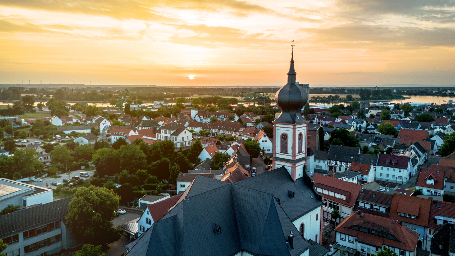 Luftbild von Gernsheim, im Vordergrund das Dach und der Zwiebelturm der Katholischen Kirche. Im Hintergrund der Rhein.
