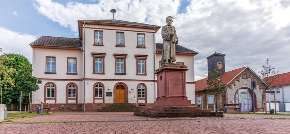 Im Vordergrund auf einem roten Sandsteinsockel befindet sich die Peter-Schöffer-Statue. Dahinter das Peter-Schöffer-Haus - ein dreigeschossiges Sandsteingebäude in dem das Museum untergebracht ist.