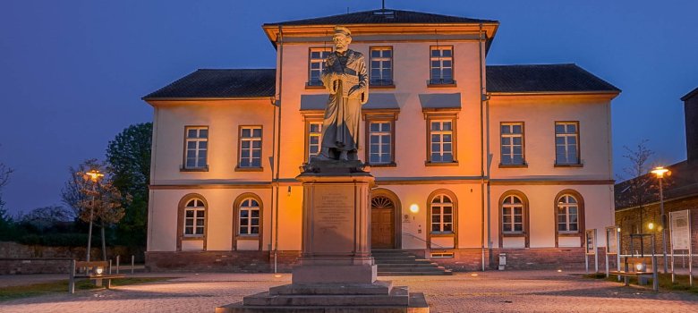 Aufnahme bei Nacht. Man sieht im Vordergrund das beleuchtete Schöffer Denkmal dahinter das Museum. Im Pflaster sind Leuchten eingebaut, die alles beleuchten. Der Himmel ist Nachtblau.