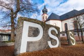 Die großen Klettersteine vor der Peter-Schöffer-Schule mit den riesigen Buchstaben P S S darauf. Im Hintergrund die Rückseite der kath. Kirche mit dem Zwiebelturm.