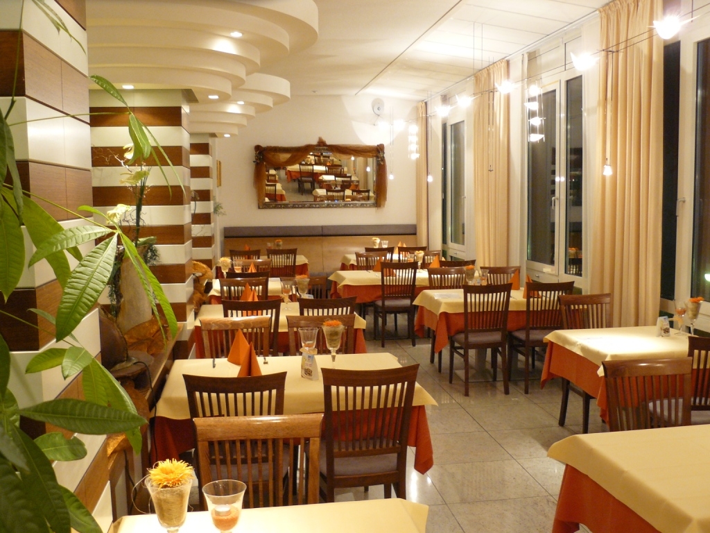 Der Gastraum des Restaurants Fontanella mit gemütlichen Tischgruppen und einem warmen rotbraun. Die Wände sind in Cremetönen angelegt auf den Tischen stehen aufrecht rostrote spitz gefaltete Servietten und Gläser mit Teelichtern.