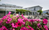 Die Stadthalle Gernsheim von vorne im Vordergrund unscharf eine Pflanze mit pinken Blüten über die hinweg fotografiert wurde.
