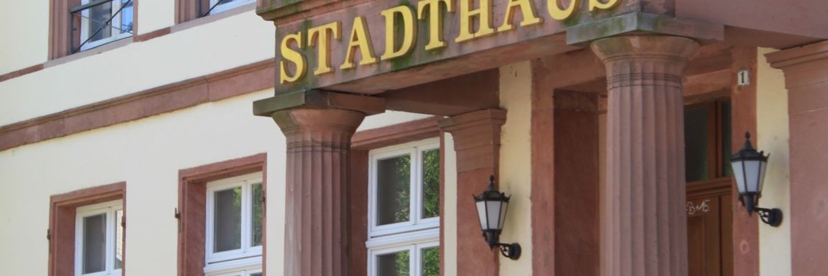 Eine schräg fotografierte Großaufnahme des Haupteingangs des Stadthauses mit eben dieser großen Beschriftung über dem Eingang im Hintergrund die Fenster des Gebäudes.