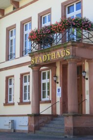 Eine schräg fotografierte Großaufnahme des Haupteingangs des Stadthauses mit eben dieser großen Beschriftung über dem Eingang im Hintergrund die Fenster des Gebäudes.