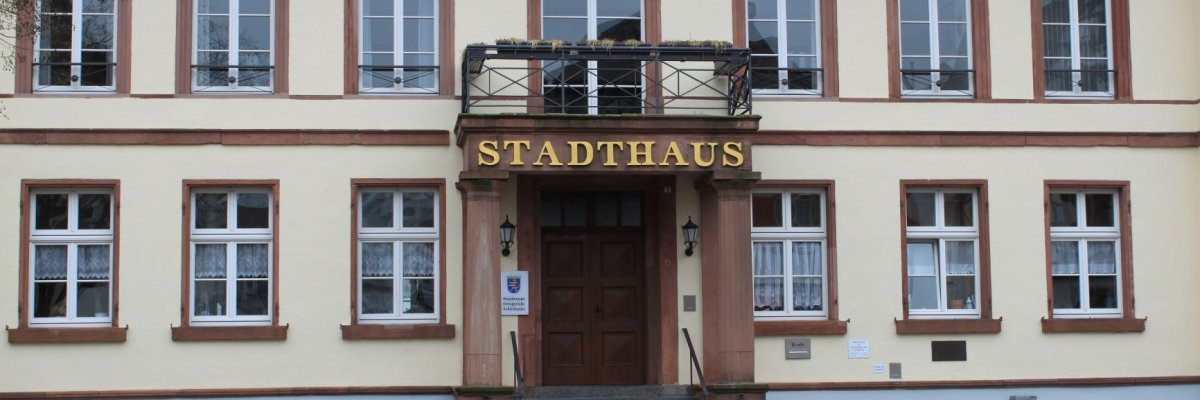 Frontale Aufnahme der Fassade des Stadthauses mittig der Haupteingang mit der großen goldenen Beschriftung STADTHAUS. Die Fassade ist cremefaqrben angelegt. Die Fensterrahmen Sandstein.