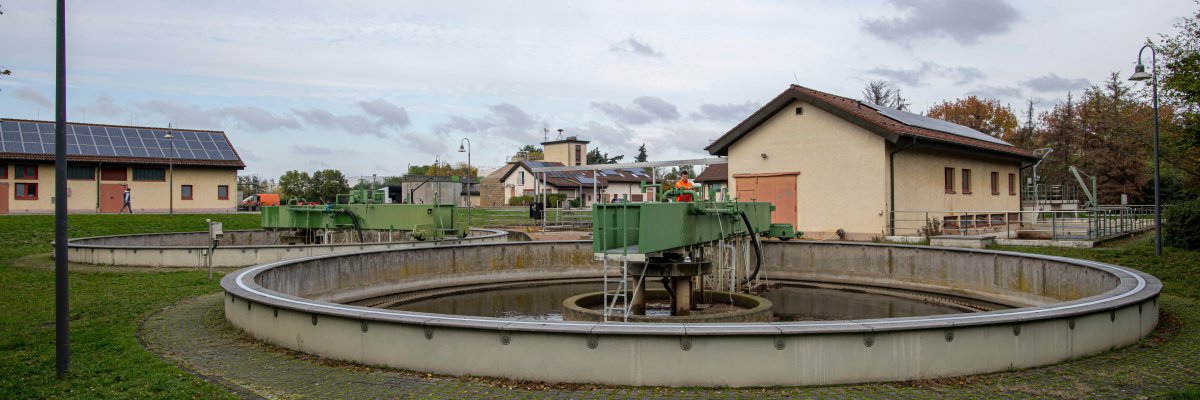 Kläranlage Gernsheim. Zu sehen ist ein Arbeiter in oranger Arbeitskleidung der am runden Klärbecken arbeitet.