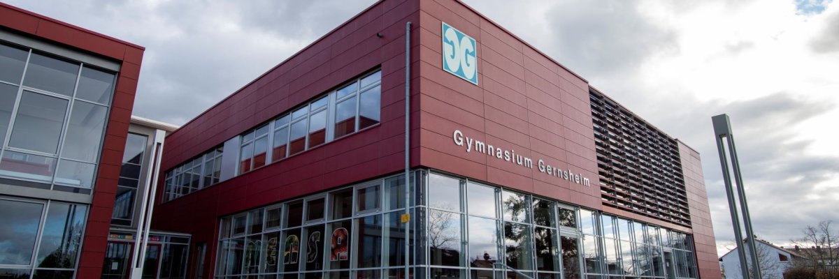 Schräg von links nach rechts verlaufender Blick auf die Front des Gymnasiums mit Hauptblick auf die Verglasung der Mensa und der großen Beschriftung des Gebäudes