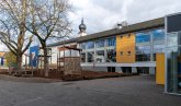 Außenspielbereich im hinter dem Gebäude gelegenen Teil der Peter-Schöffer-Schule mit Blick auf das Schulgebäude und dem dahinter ausragenden Zwiebelturm der katholischen Kirche