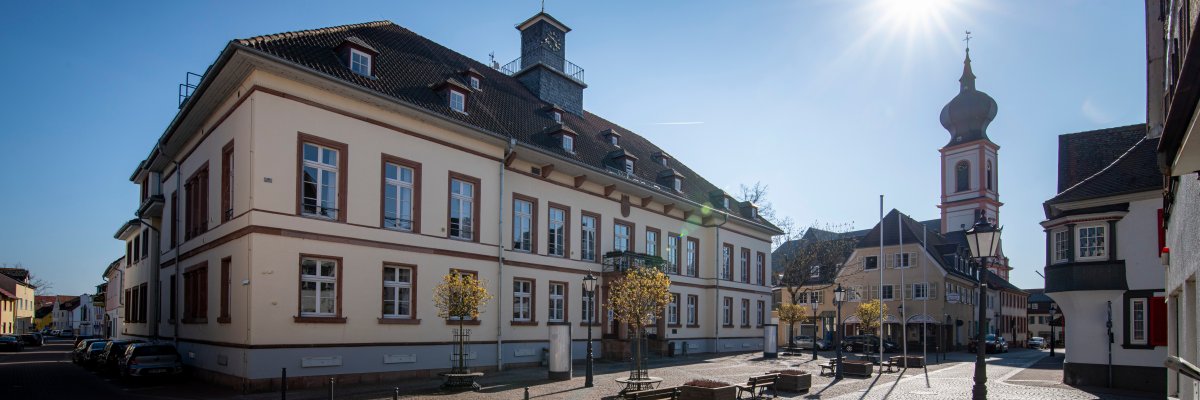 Das Stadthaus Gernsheim aus Richtung der Brasserie aufgenommen Man sieht die katholische Kirche über der die Sonne scheint, der Himmel ist freundlich