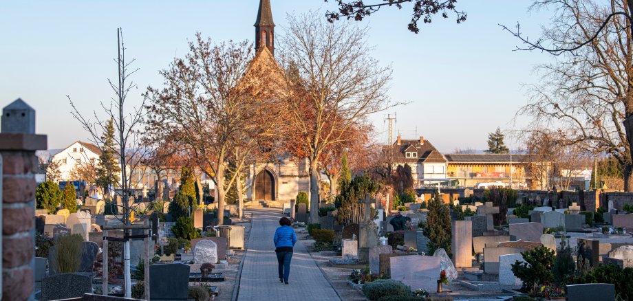 Im Vordergrund befinden sich mehrere Grabsteine des Friedhofs Gernsheim. Im Hintergund befindet sich hinter zwei Bäumen die Michaeliskapelle des Friedhofs.