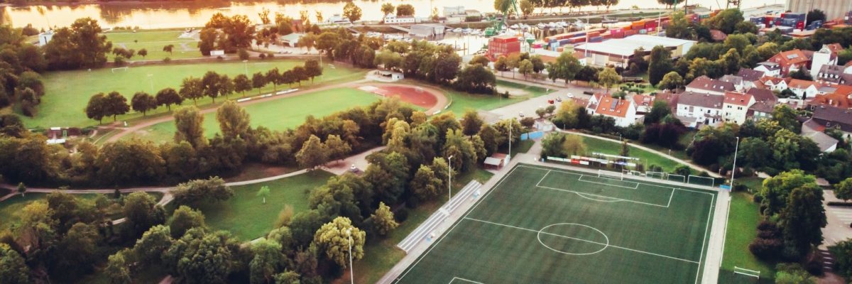 Drohnenbild des Sportgeländes Am Kaffeedamm links die Laufbahn rechts der Kunstrasenplatz im Hintegrund geht die Sonne in Richtung Pfalz unter man sieht den Hafenbereich und Waibel am rechten Bildrand