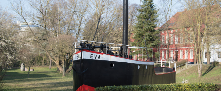 Das Bild zeigt den Aalschokker Eva. Ein Schiff das auf dem Rhein zum Fischfang genutzt wurde. Es ist hauptsächlich schwarz, hat über den Bullaugen eine  weißen Streifen auf dem der Name Eva steht und am Rand der Reling einen roten Streifen. Oben auf dem Deck sieht man Maschinerie und einen dicken schwarzen Mast.