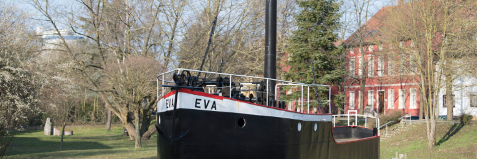 Das Bild zeigt den Aalschokker Eva. Ein Schiff das auf dem Rhein zum Fischfang genutzt wurde. Es ist hauptsächlich schwarz, hat über den Bullaugen eine  weißen Streifen auf dem der Name Eva steht und am Rand der Reling einen roten Streifen. Oben auf dem Deck sieht man Maschinerie und einen dicken schwarzen Mast.