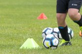 rechts im Bild Kinderbeine in Fußballkleidung bei dribbeln eines Fußballs auf Rasen um gelbe Markierungen herum
