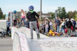 Kind mit Helm und Roller mit dem Rücken zur Kamera steht auf einem Element der Skaterbahn am Rhein. Im Hintergrund sieht man unscharf den Auszeitbus mit vielen Kindern und Jugendlichen davor.