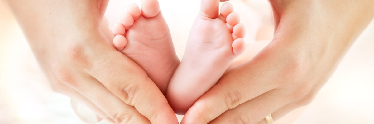 Zwei Hände formen ein Herz. In deren Mitte sind zwei Babyfüße zu sehen.