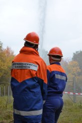 Zwei Mitglieder der Jugendfeuerwehr mit Helmen und blau orangener Schutzkleidung Löschen bei einer Übung.