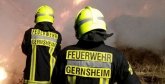 Drei Einsatzkräfte der Feiwilligen Feuerwehr Gernsheim löschen bei einem nächtlichen Einsatz einen Heuhaufen. Rauch steigt aus der Mitte des Bilds auf. Man sieht kleine Flammen am Boden.