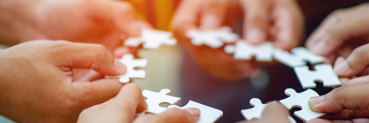 Zehn Hände halten jeweils ein weißes Puzzelteil zu einem Kreis.