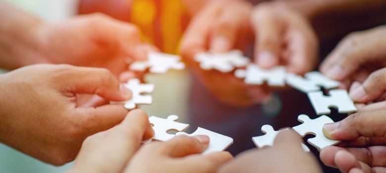 Zehn Hände halten jeweils ein weißes Puzzelteil zu einem Kreis.