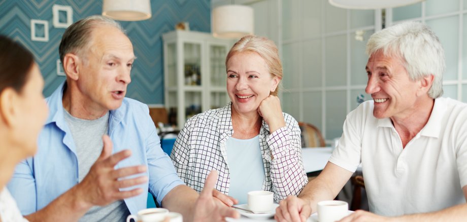 Zwei ältere Männer und zwei ältere Frauen unterhalten sich bei einer Tasse Tee an einem Tisch in einem Café.