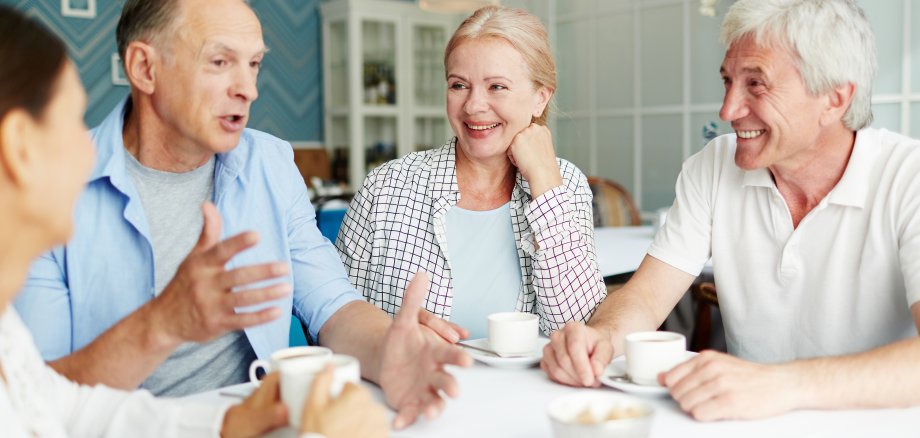 Zwei ältere Männer und zwei ältere Frauen unterhalten sich bei einer Tasse Tee an einem Tisch in einem Café.