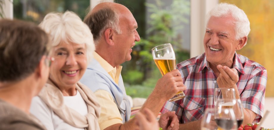 Zwei Seniorinnen und zwei Senioren sitzen an einem Tisch und unterhalten sich. Auf dem Tisch steht Essen und Trinken.