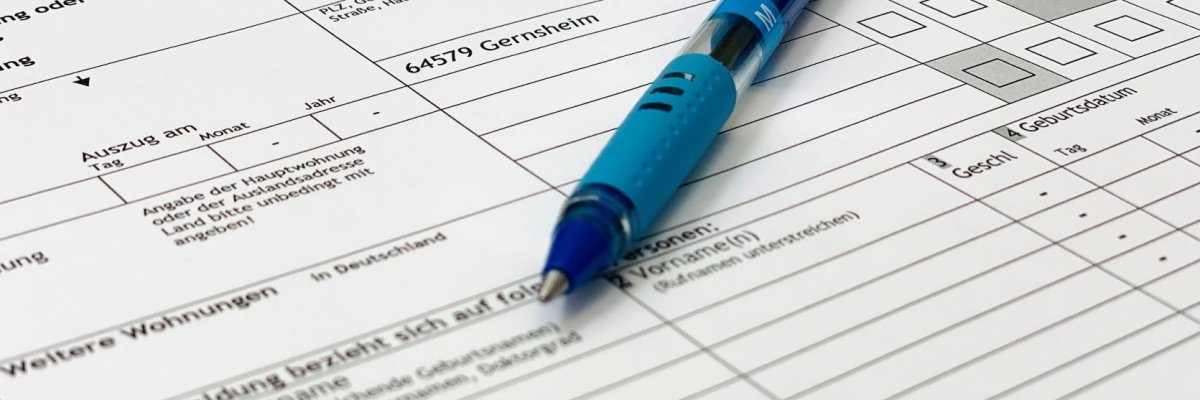Ein Formular zur Anmeldung beim Einwohnermeldeamt liegt schräg im Bild. Darauf ein blauer Kugelschreiber.