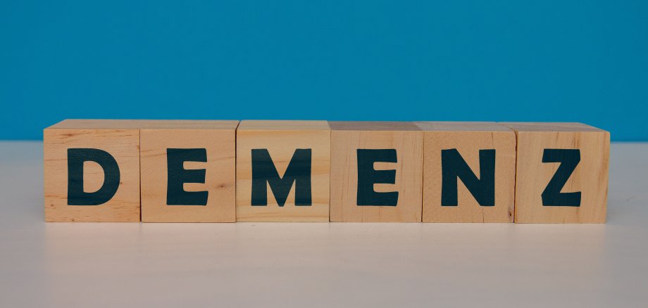 Sechs Holzwürfel mit Buchstaben liegen auf einem Tisch und ergeben das Wort Demenz.