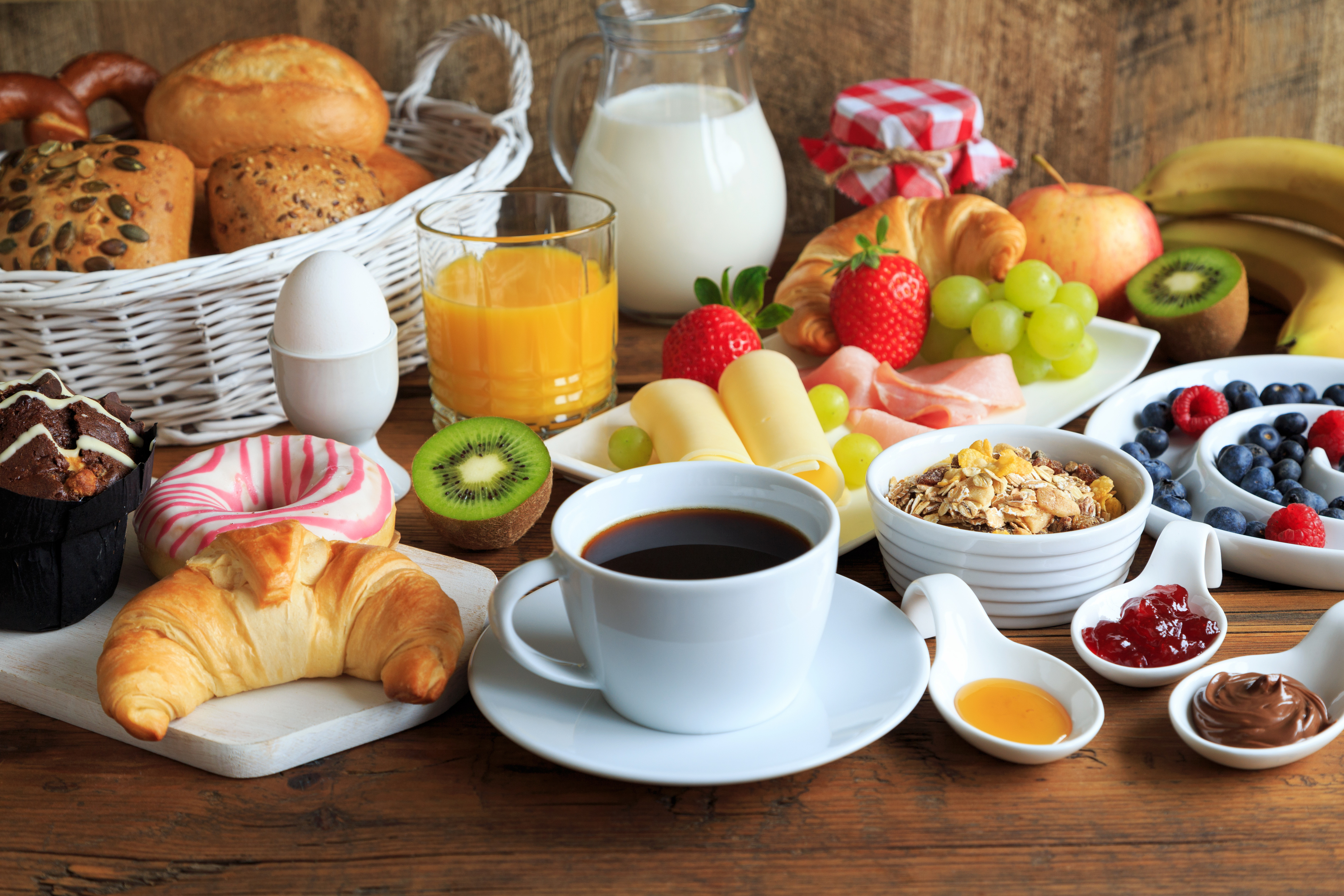 typischer Frühstückstisch mit Kaffee, Marmelade, Brötchen, Croissant, Ei und Obst