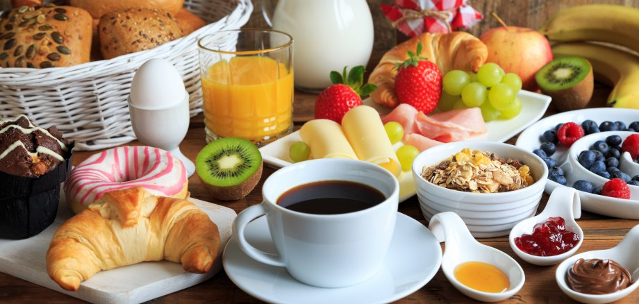 typischer Frühstückstisch mit Kaffee, Marmelade, Brötchen, Croissant, Ei und Obst