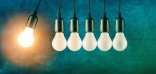 Impetus Vor einem blau-grünen Hintergrund sind fünf hängende Glühbirnen in Reihe mit schwarzer Fassung und einem schwarzen Stück Kabel als Lampe zu sehen. Die linke sechste Glühbirne pendelt nach links und leuchtet. Sie hat einen kreisförmigen, orangefarbigen runden Hintergrund.
