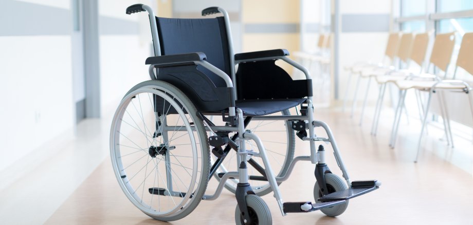 In einem Wartebereich mit Stühlen eines Krankenhausflures steht ein Rollstuhl.